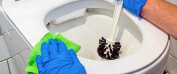a person wearing gloves and cleaning toilet rim jets with sponge