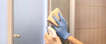 a person cleaning shower door with sponge while wearing gloves